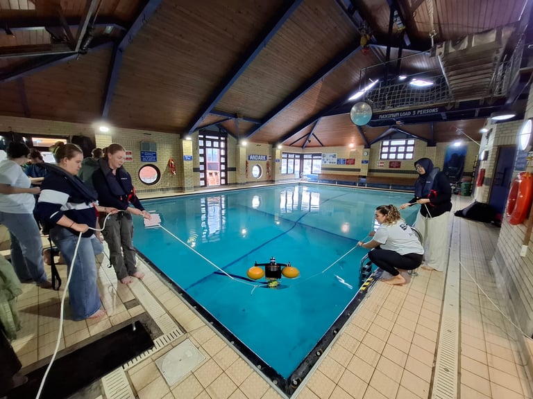 Four students lower an acoustic receiver into a pool on ropes
